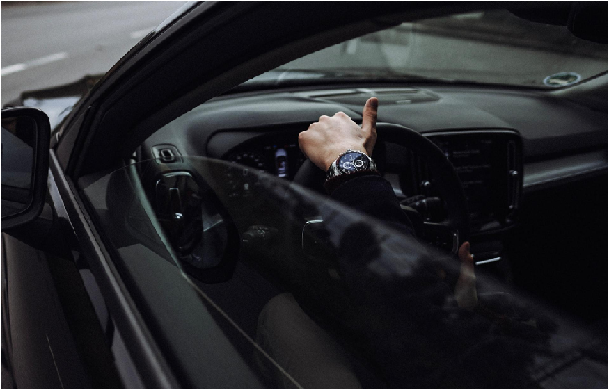 A close-up picture of someone’s hand on the steering wheel of their car as they drive down the road